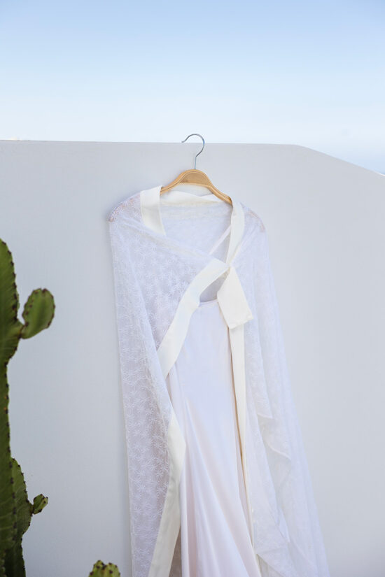 An elegant wedding dress hanging on a whitewashed wall at Omna Caldera Suites.