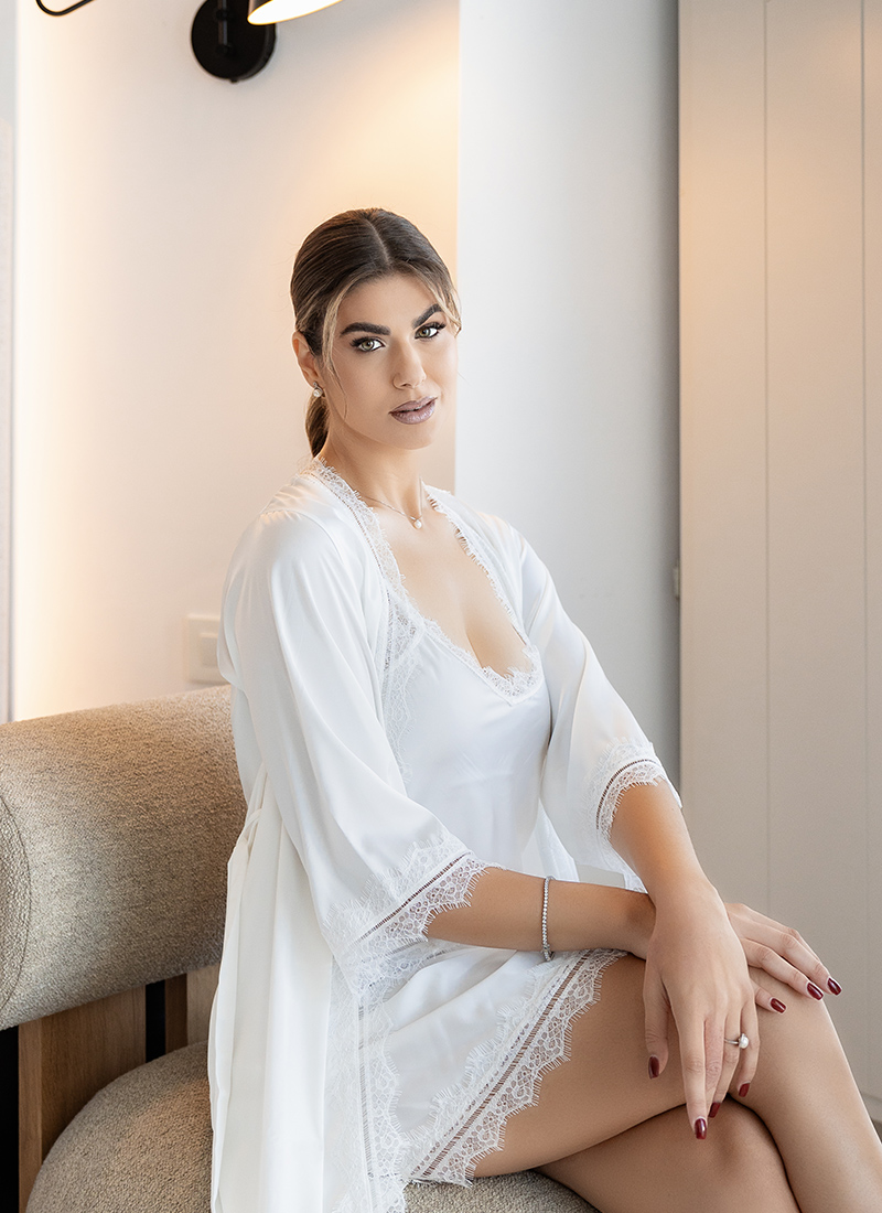 A bride wearing a white satin nightgown, staring at the camera at Omna Caldera Suites.