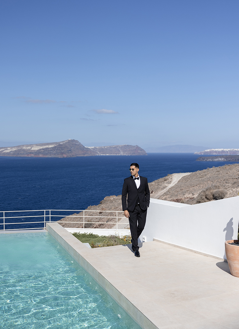 A groom walking by a pool, admiring the sea view at Omna Caldera Suites in Santorini.