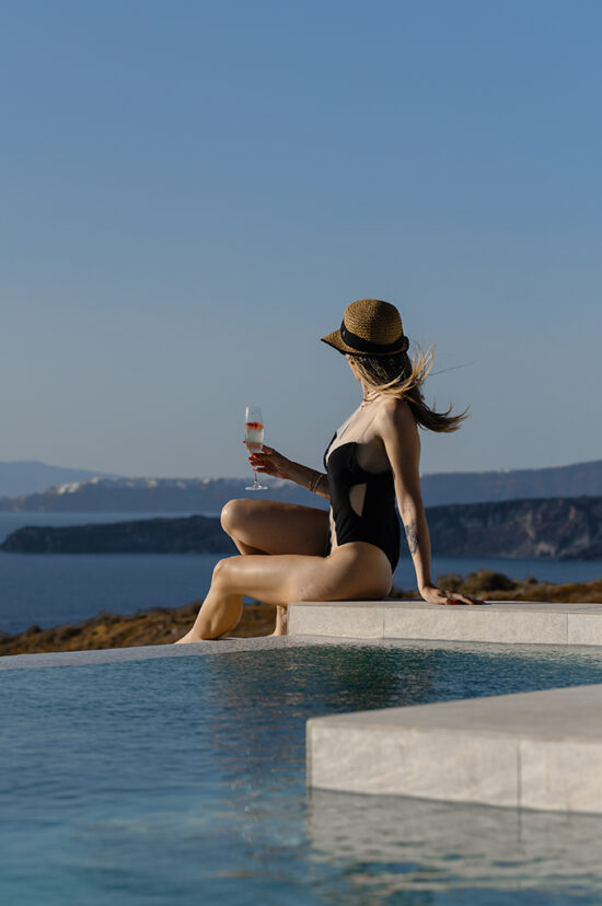 Lady in a swimsuit sitting by the pool overlooking the sea at Luxury Suites in Santorini.