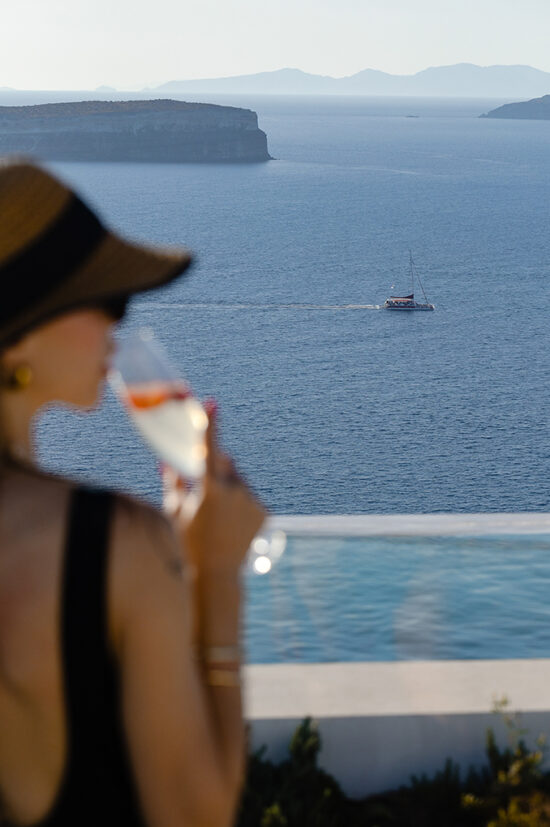 A lady enjoying a drink overlooking the pool and the sea at the Luxury Suites in Santorini.